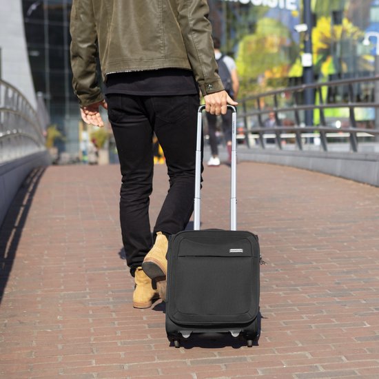 Man met zwarte broek en bruine schoenen rolt een zwarte "CarryOn" koffer met trekstang.