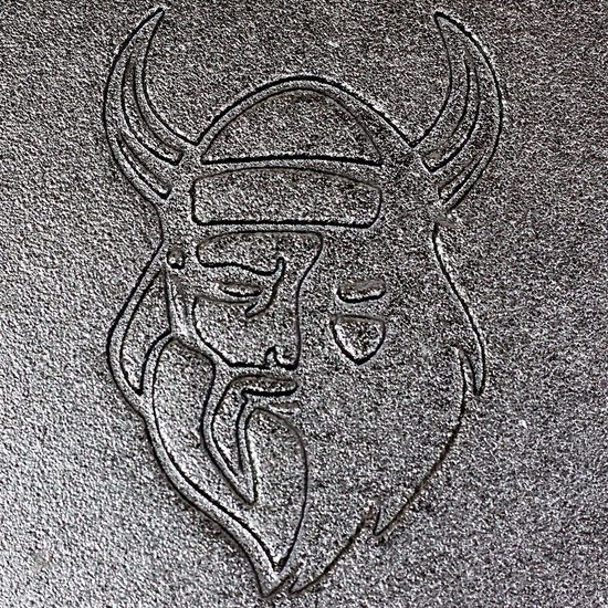 Gedetailleerd reliëf van een Viking-hoofd met hoorns op een gegoten oppervlak.