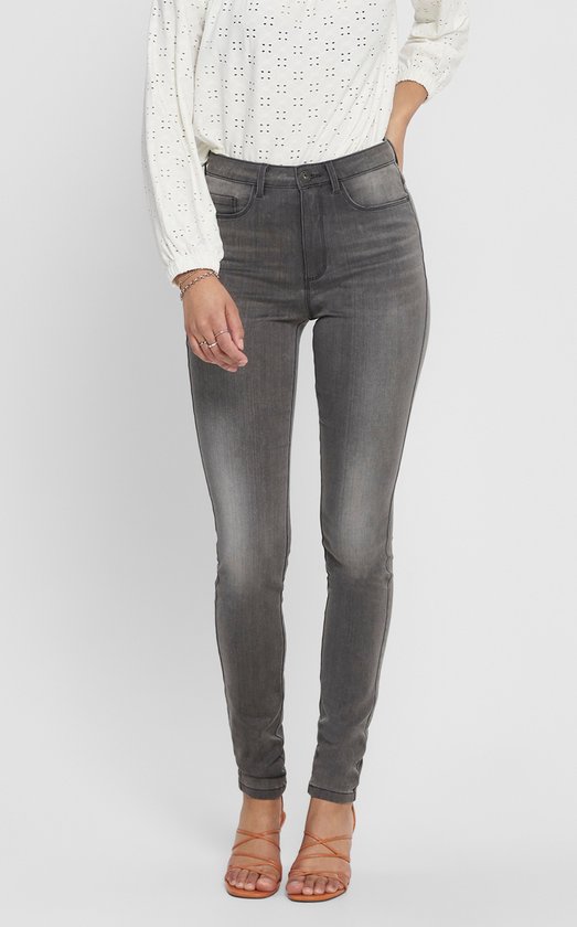 Model draagt een grijze skinny jeans met een witte geborduurde blouse.