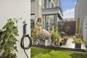 Vrouw met spuitmond op tuinslang, buiten bij bloemen en een opgerolde zwarte tuinslang aan een Gardena houder.