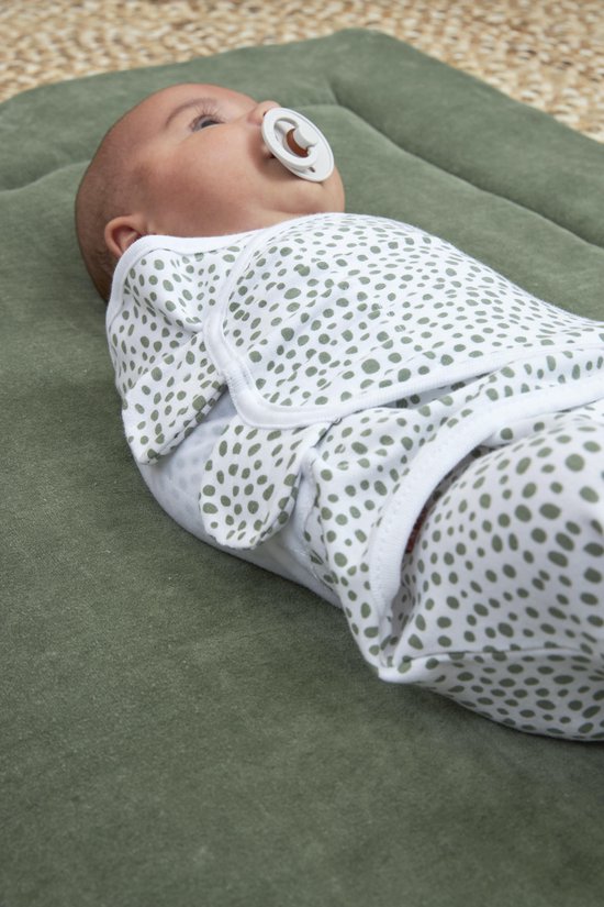 Baby ingebakerd in een effen groene inbakerdoek, liggend op een groen kleed.