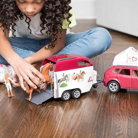 Meisje speelt met roze auto, paardentrailer met paarden, ruiter en paard dat de trailer ingaat.