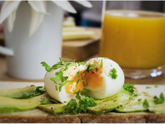 Gekookt ei op toast met avocado, gegarneerd met peterselie en peper.