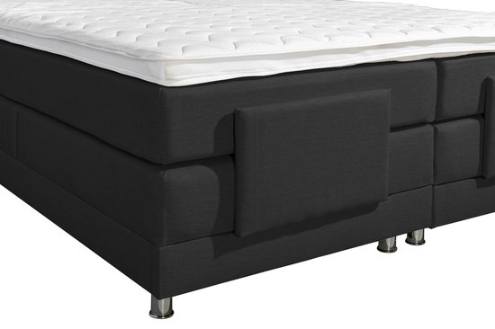 Gedetailleerde opname van een zwart boxspringbed met opbergvakken en chromen pootjes, met een deel van het witte matras.
