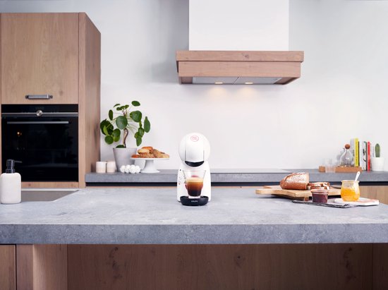 Witte Krups Dolce Gusto Piccolo XS koffiecupmachine in een moderne keuken, met een kopje koffie erop.