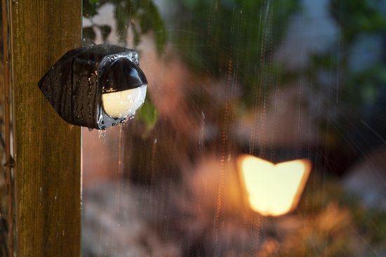 Zwarte bewegingssensor op een houten paal, met regen op de lens.