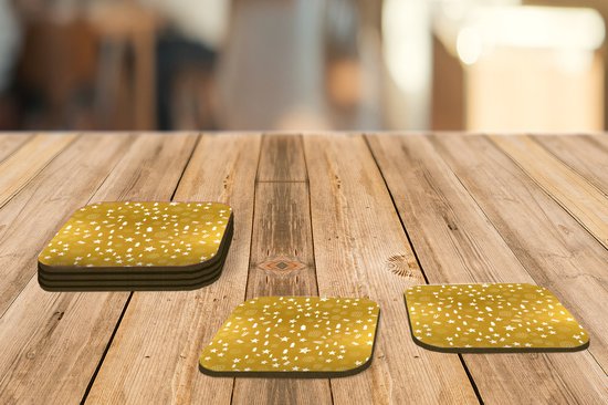 Sous-verres dorés avec un motif blanc d'étoiles, de sapins et de rayures, sur une table en bois.