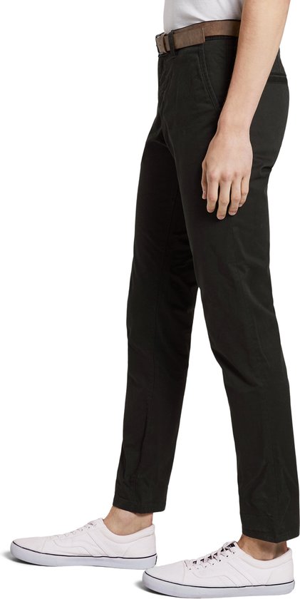 Man in zwarte chino, zijkant zichtbaar, met bruine riem en witte sneakers.