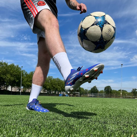 Soulier de football bleu avec étoiles rouges, chaussettes blanches avec logo noir, à côté d'un ballon de football.