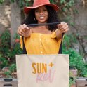 Vrolijke vrouw met zonnehoed en gele top die een SUN+Rev tote bag vasthoudt.