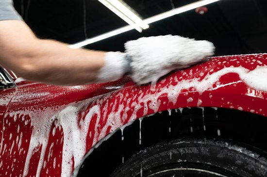 Man wast de rode auto met schuimende shampoo. Close-up op het spatbord en de wielkast.