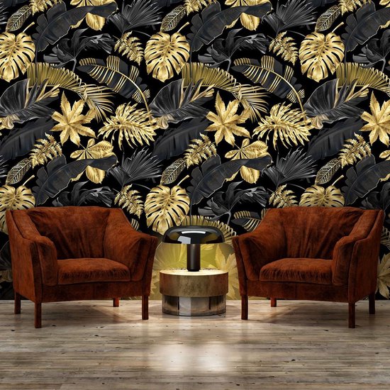 Gouden en zwarte jungle bladeren op een zwart behang, achter twee bruine fauteuils bij een bijzettafel.