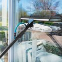 Raamwisser met witte doek op een telescoopsteel, raamt water af. Groene slang aanwezig.