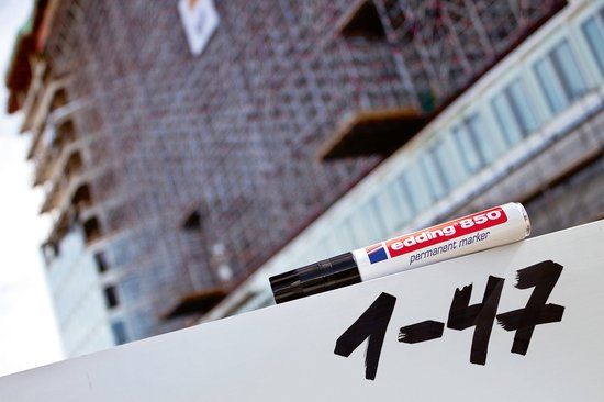 edding 850 permanente marker op een wit oppervlak met de tekst '1-47' ernaast, bouwplaats op achtergrond.