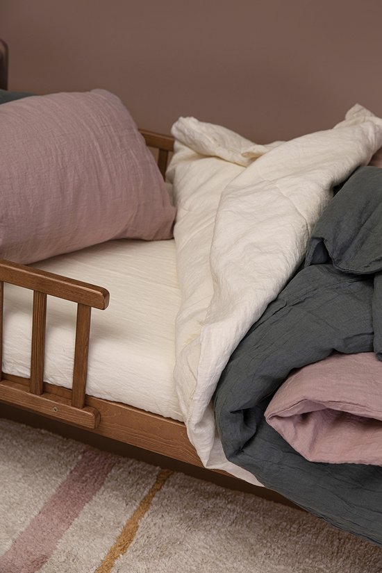 Houten kinderbed met linnen beddengoed in off-white, oudroze en donkergroen. Met gebloemde sprei.