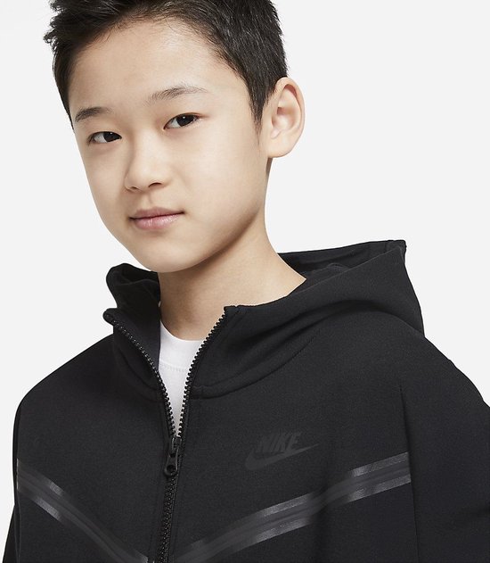 Jongen in een zwart Nike Tech Fleece vest met capuchon, deels open geritst.