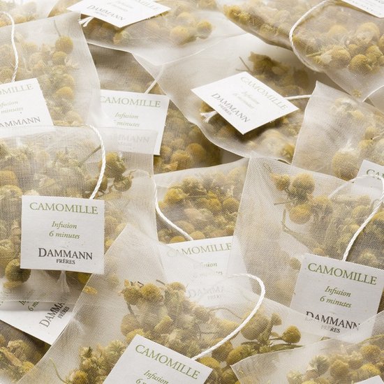 Close-up van meerdere witte Dammann Frères theezakjes gevuld met gedroogde kamillebloemen.