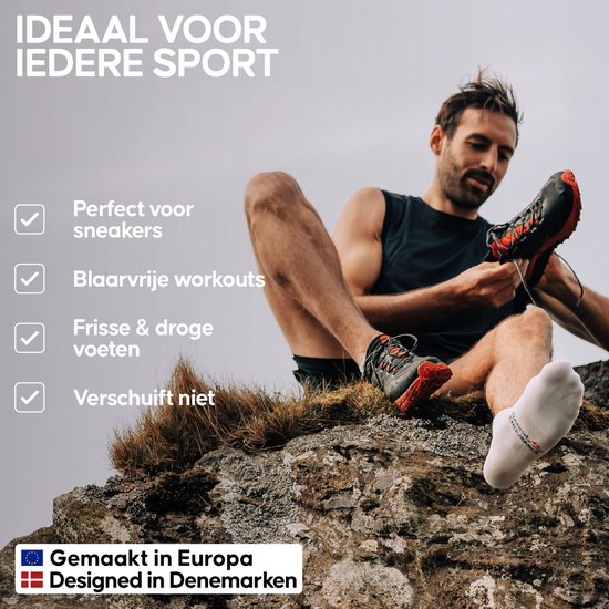 Man met donkere huidskleur, die een sportschoen aantrekt en een witte sok draagt, zittend op rots.
