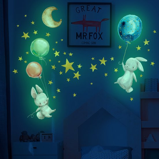 Sticker mural phosphorescent : deux lapins flottent avec des ballons parmi des étoiles, une lune et une planète.