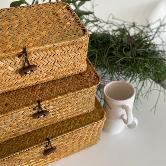 Trois boîtes de rangement en rotin empilées avec couvercles et fermetures à bouton en bois.