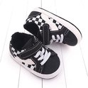 Babyschoentjes met zwart-wit dambordpatroon, klittenbandsluiting en witte veters. Zijkant met wit accent.