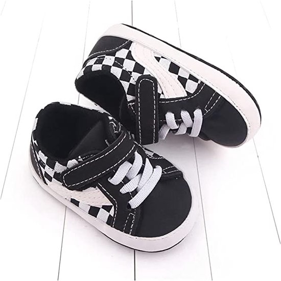 Babyschoentjes met zwart-wit dambordpatroon, klittenbandsluiting en witte veters. Zijkant met wit accent.