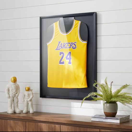 Geel basketbalshirt van de Lakers met nummer 24, ingelijst in een zwarte lijst tegen een lambrisering.