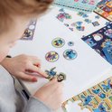 Enfant collant un autocollant de Stitch et Lilo sur une feuille de papier blanche. Plus d'autocollants sont sur la table.