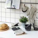 Keukenblad met brood, mortier, potplant, fles en twee pannenlappen: één om de hand en twee kleine.