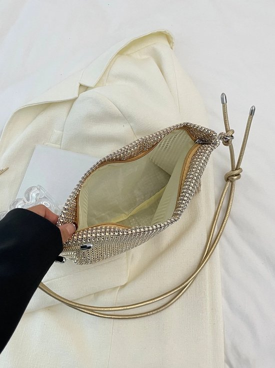 Open gouden metallic clutch tas die wordt vastgehouden, met een goudkleurige band.