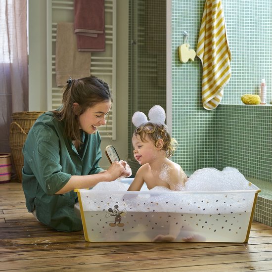 Vrolijk gezin met een baby in een schuimbad in een transparante badkuip met Mickey Mouse-print.