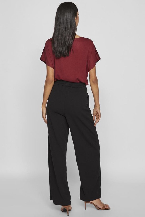 Model van achteren in bordeauxrode top en wijde zwarte broek met hoge taille.