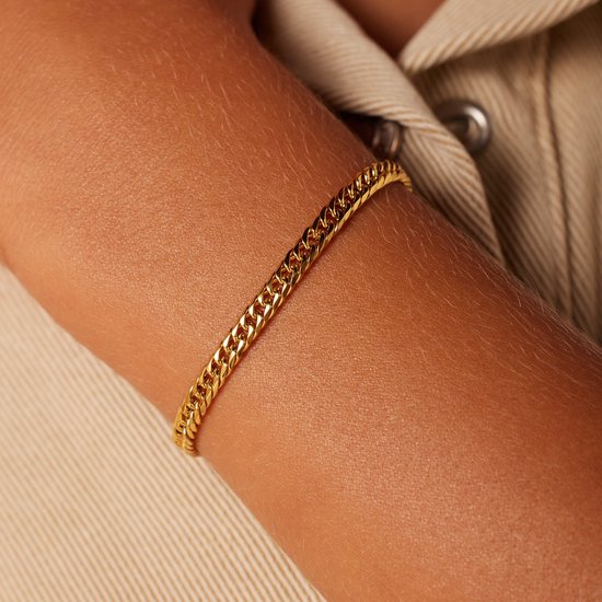 Close-up van een gouden armband met gourmetschakel om een arm.