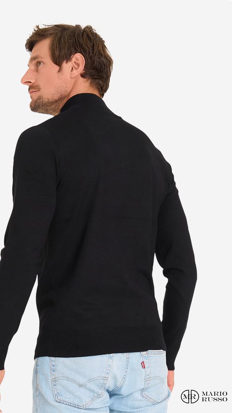 Achterkant van een man in een zwarte trui met rits en lichtblauwe jeans.