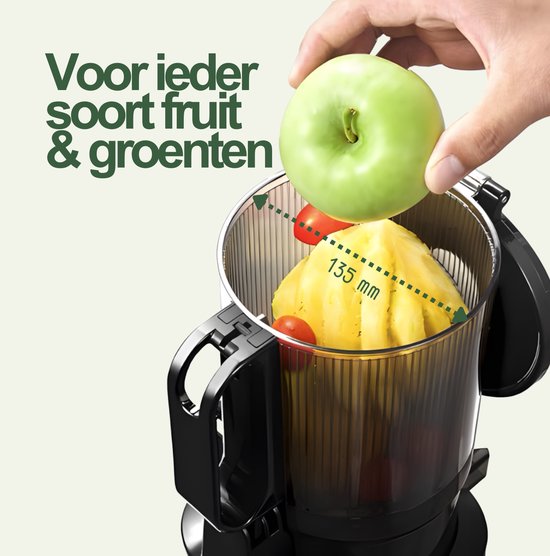 Une main ajoute une pomme verte à une grande centrifugeuse lente noire contenant de l'ananas et des tomates cerises. La largeur d'entrée de 135 mm est indiquée.