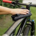 Hand veegt met donkere doek over een zwarte fiets met natte vlekken.