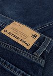 Close-up van het bruine leren label van G-Star Raw op een donkerblauwe spijkerbroek. Het label bevat tekst en logo.
