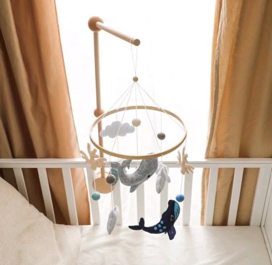 Houten babybed hanger met vilten decoraties: grijze walvis, blauwe walvis, mintgroene walvis, wolken, koraal en ballen, hangend boven een ledikant.