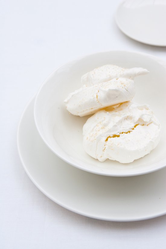 Witte kom met twee meringuekoekjes erin, staand op een witte schotel.