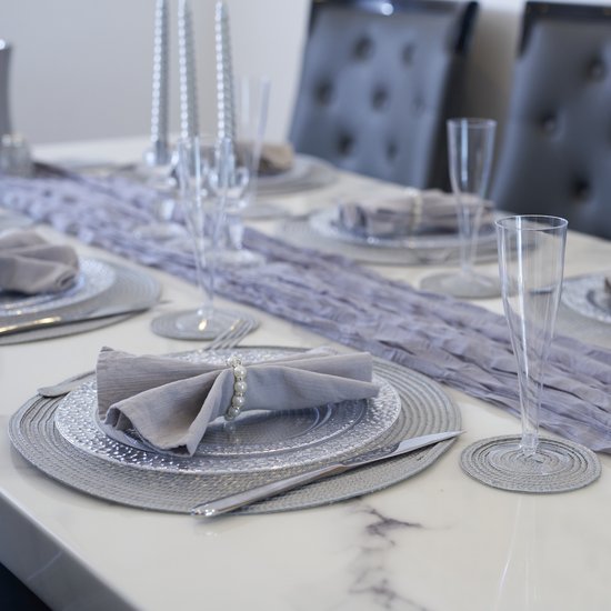 Gedekte tafel met zilveren placemats, glazen, bestek en een lila tafelloper.