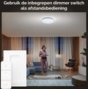 Een vrouw doet yoga in een woonkamer verlicht door een Philips Hue Enrave plafondlamp. Naast de lamp, een dimmer switch.