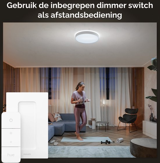 Een vrouw doet yoga in een woonkamer verlicht door een Philips Hue Enrave plafondlamp. Naast de lamp, een dimmer switch.