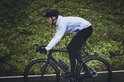 Man op een racefiets in de regen, draagt een doorschijnende witte fietsregenjas, zwarte fietsbroek en helm.