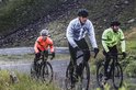 Drie fietsers rijden op een weg in de regen. Eén draagt een witte regenjas, één een neongele en één een oranje.