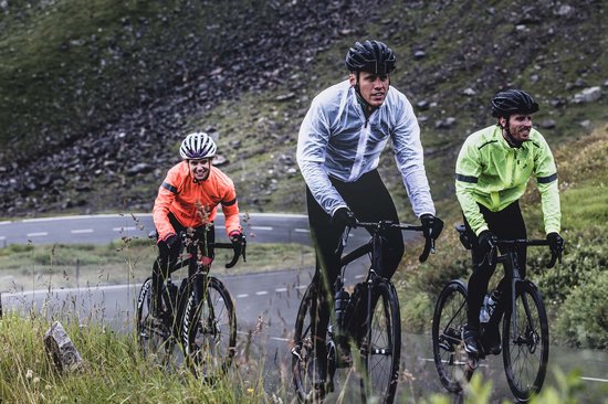 Drie fietsers rijden op een weg in de regen. Eén draagt een witte regenjas, één een neongele en één een oranje.