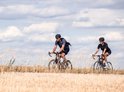 Man en vrouw fietsen op een droge akker onder een bewolkte hemel.