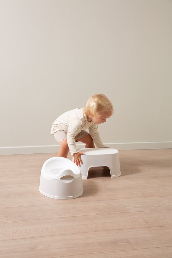 Une jeune fille aux couettes blondes se penche vers un marchepied blanc à côté d'un pot blanc.