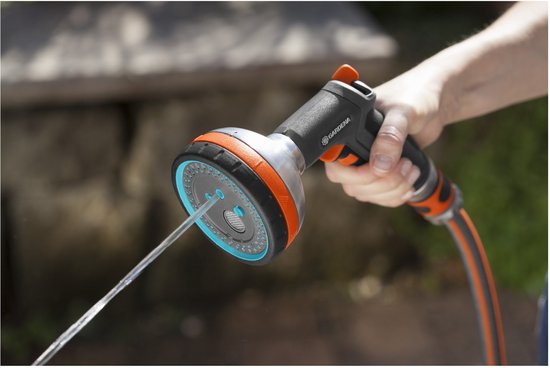 Een hand houdt een grijze Gardena sproeikop vast, water spuitend op de grond.