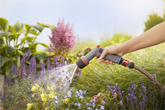 Hand sproeit bloemen in een tuin met een Gardena spuitpistool.