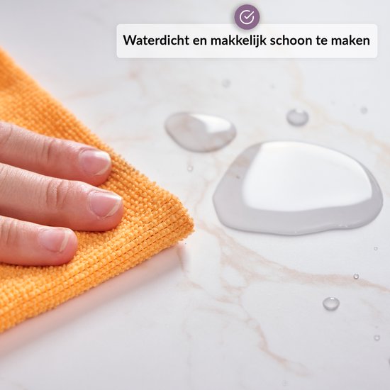 Hand veegt waterdruppels weg van een marmeren achtergrond met een oranje doekje.
